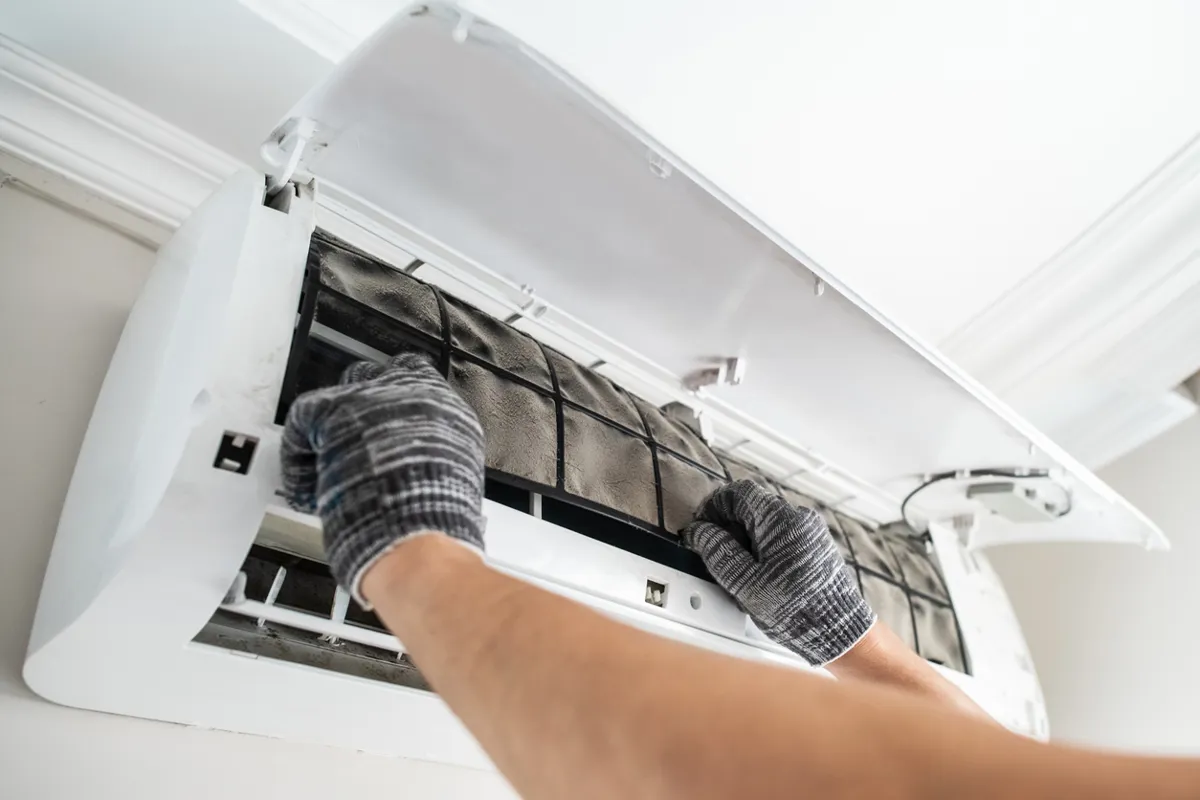  Technician replacing a dirty air filter of an air conditioner indoors.