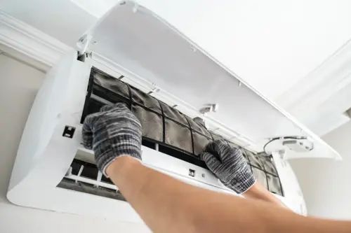Technician replacing a dirty air filter of an air conditioner indoors.