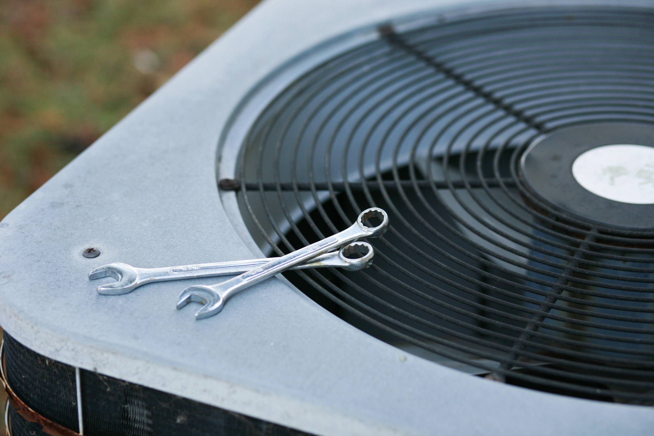 An image of an outdoor AC unit with wrenches on the top, which belong to an HVAC technician about to repair the unit.